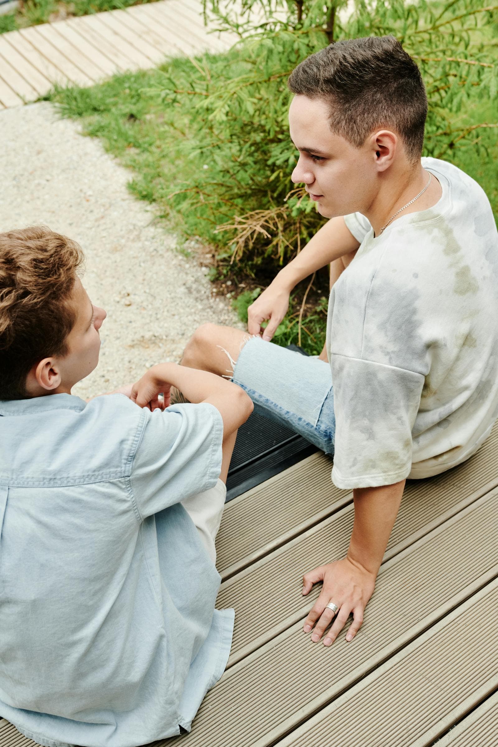 Two young men sitting outside in conversation, looking at each other