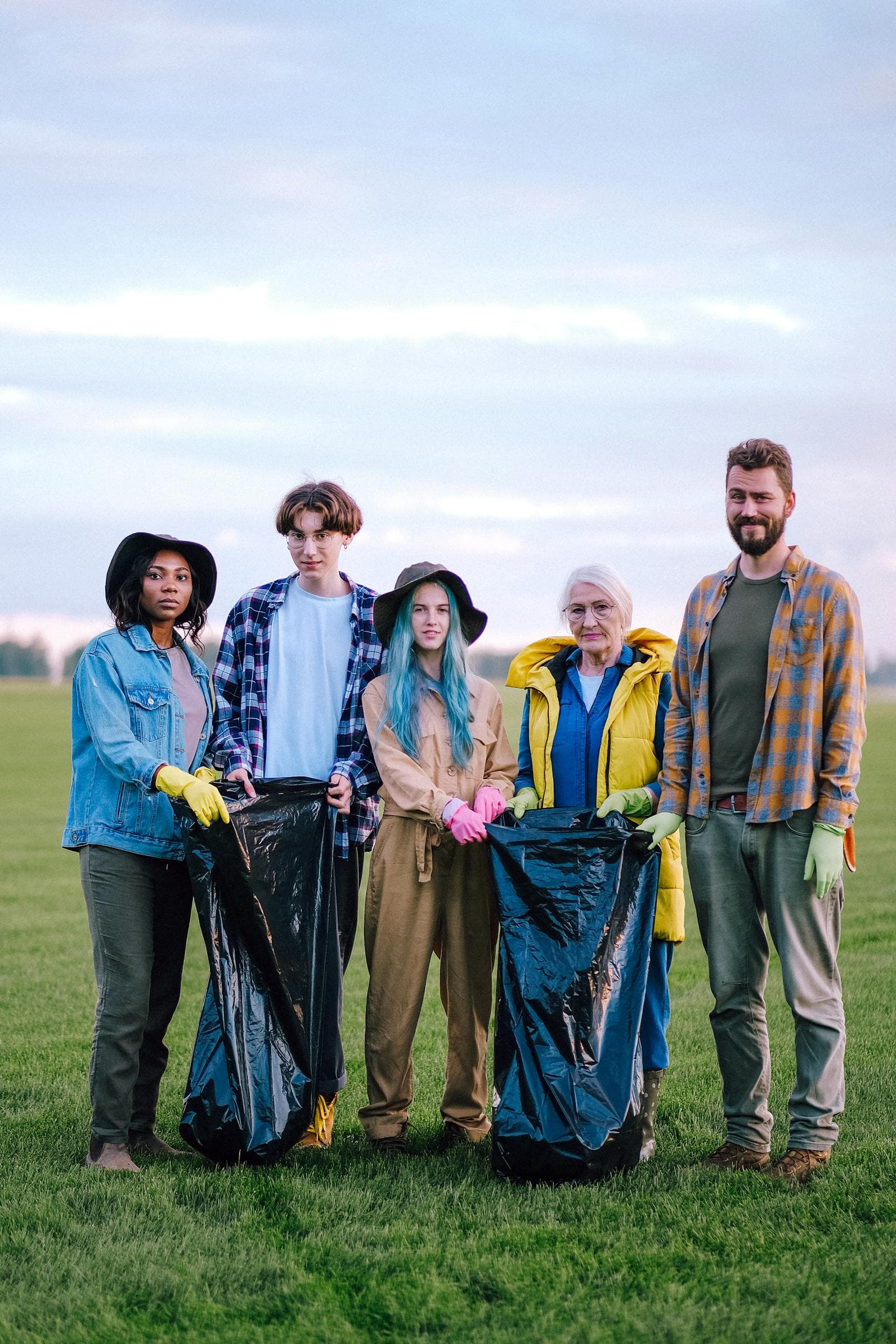 A multi-generational group of community volunteers standing together in a field after collecting waste